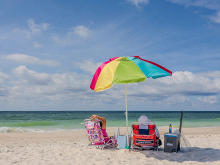 A couple sitting under a rainbow beach umbrella on the beach in Gulf Shores