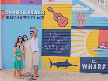 Family taking a selfie in front of The Wharf mural