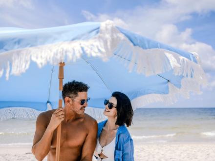 Couple standing under a blue beach umbrella on the beach in Gulf Shores
