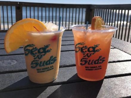 Two coastal cocktails sitting on a table facing the beach at Sea-N-Suds