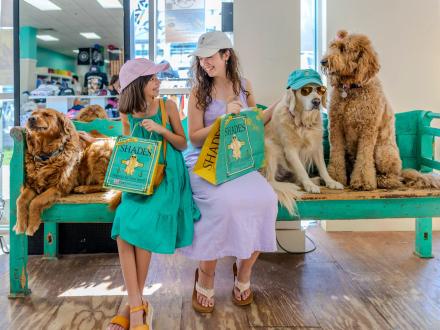 Girls sitting with dogs and shopping bags at Shades Sunglasses & Casual Apparel at The Wharf
