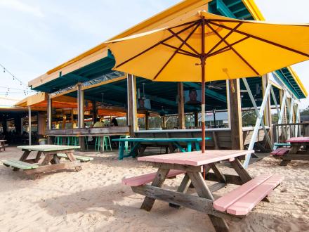 Picnic tables with umbrellas in the sand at LuLu's family-friendly restaurant in Gulf Shores