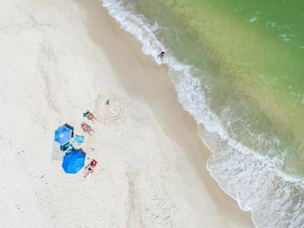 Aerial view of a family sitting under bright umbrellas near the water in Orange Beach