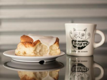 Big cinnamon roll on a plate next to a mug of coffee at BuzzCatz in Orange Beach