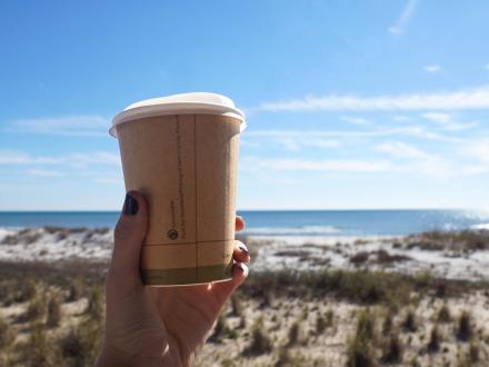hand holding a to-go cup of coffee at the beach at The Lodge Hotel in Gulf Shores