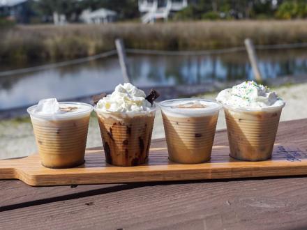 A flight of iced coffee sitting on a table in front of the water at High Tide
