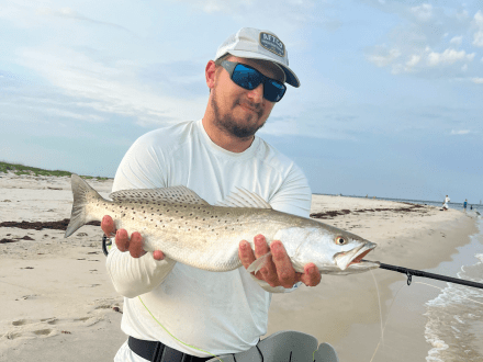 Man holding a speckled trout caught while surf fishing in Orange Beach