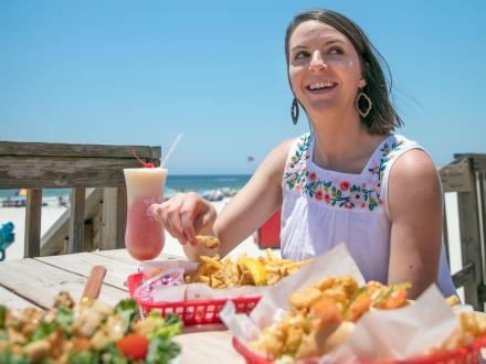 Woman dining at a picnic table full of food on the deck at Pink Pony Pub beachfront bar in Gulf Shores