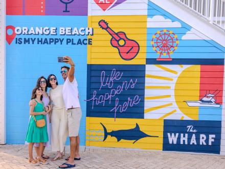 Family snapping a selfie in front of the mural at The Wharf in Orange Beach
