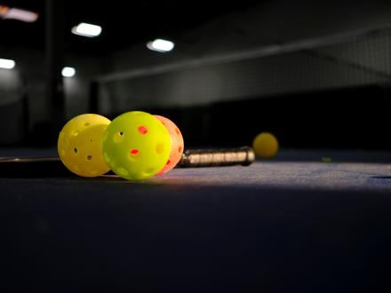 pickleballs and a paddle laying down on an indoor pickleball court