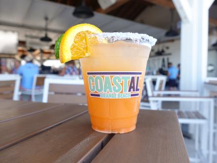 bright orange margarita with a salted rim sitting on a table in the outdoor dining area at Coastal beachfront restaurant in Orange Beach