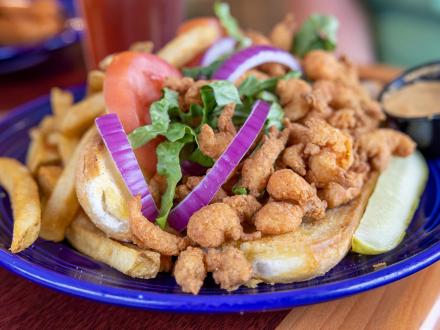 a delicious fried shrimp poboy dresses with lettuce, tomatoes, and red onions on a blue pate at Desoto's seafood restaurant in Gulf Shores