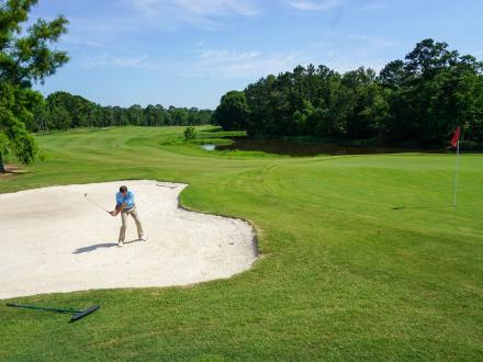 Golfer swinging a club in a sand pit on the golf course at Craft Farms