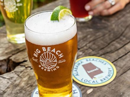 a pint glass full of a light beer sitting on a wooden table at Big Beach Brewing in Gulf Shores
