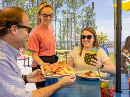 Waitress putting down a seafood boil plate in front of a couple dining outside at GTs on the Bay seafood restaurant