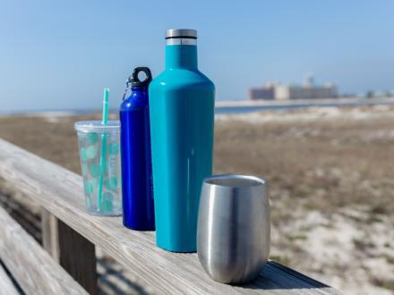 line a various resusable cups and bottles sitting on the side of a boardwalk leading to the beach in Orange Beach