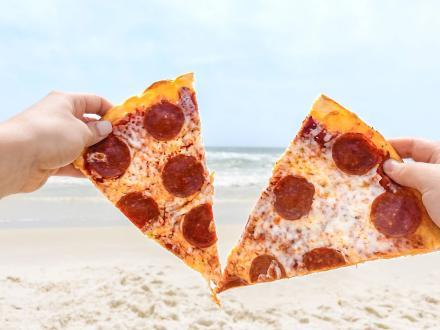 Hands holding two big slices of pepperoni pizza at the beach in Orange Beach