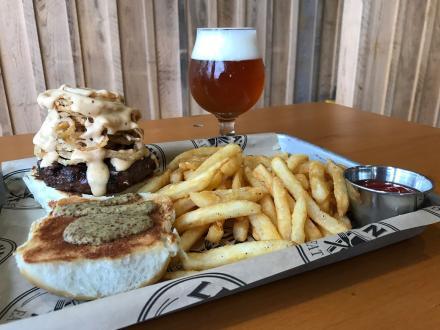 a giant burger topped with onion rings, French fries, and a pint of beer on a table at Luna's
