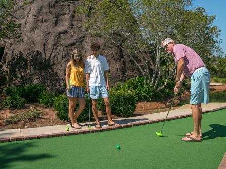 Mom and son watching dad hit a ball during a game of putt putt at Adventure Island, mini golf and arcade in Orange Beach