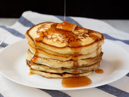 Stack of pancakes with a slice of butter on top and syrup drizzling over them