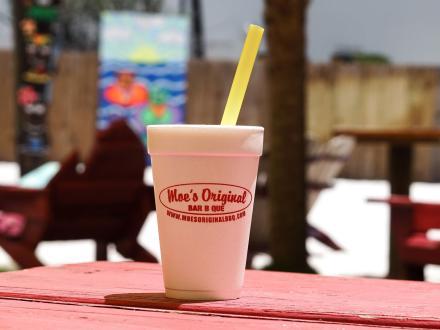 a bushwacker sitting on a picnic table at the backyard beach of Moe's barbecue restaurant in Orange Beach