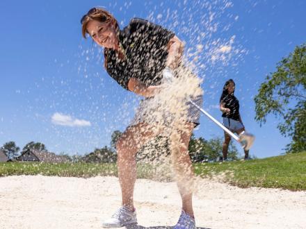 golfer hitting a ball out of a sand trap on a course in Gulf Shores
