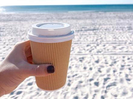 hand holding a cup of coffee on the beach