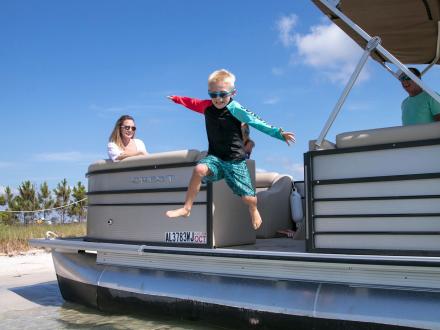 young boy jumping out of a pontoon boat rental into the water in orange beach