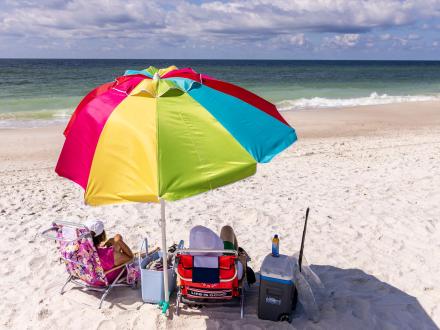 snowbird couple relaxing under a rainbow beach umbrella near the water in Orange Beach