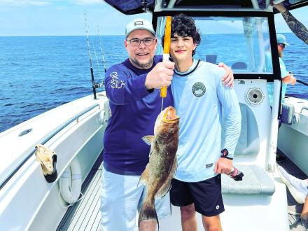 Man and son holding up a grouper caught on an offshore charter trip in Orange Beach