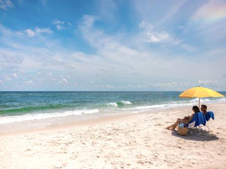 Couple sitting on the beach under a beach umbrella in Gulf Shores