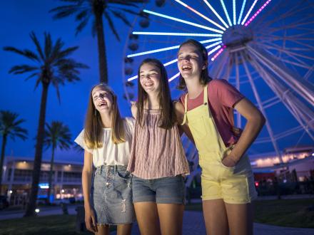 Girls posing in front the Ferris wheel at the wharf lit up at night