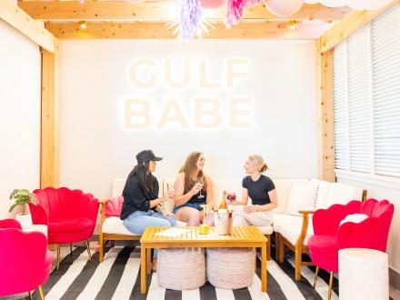 Three girlfriends sitting on the couch with drinks at Gulf Babe wine boutique at The Wharf