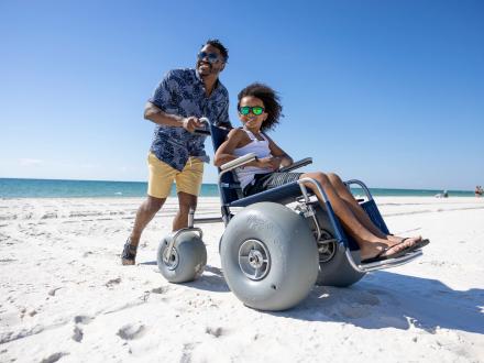 Dad pushing son in electric wheelchair along the beach in Gulf Shores