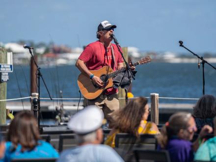 Musician performing by the water during the Annual Meeting of the Minds event in Orange Beach