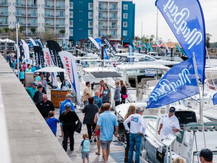 People walking along the marina lined with boats at the Wharf Boat & Yacht Show in Orange Beach