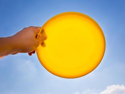 hand holding a yellow frisbee in the sky