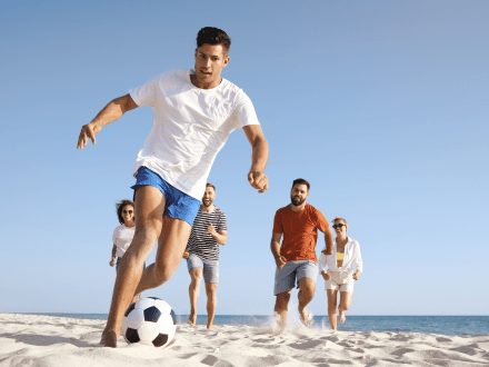 People playing soccer on the beach by the shoreline