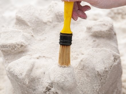 Hand brushing off loose sand from a sandcastle on the beach
