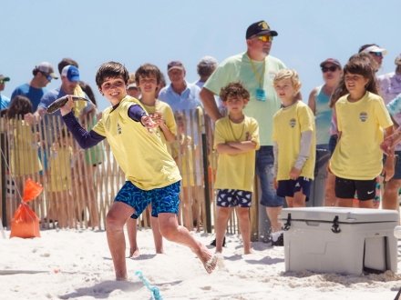 Kid throwing a fish on the beach at the Annual Flora-Bama Mullet Toss