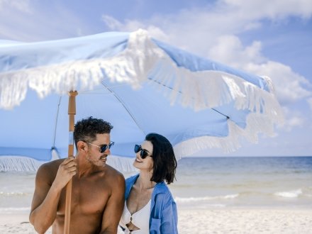 Couple standing under a blue beach umbrella on the beach in Gulf Shores