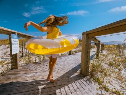 Young girl running on a boardwalk with a pool float toward the beach in Gulf Shores