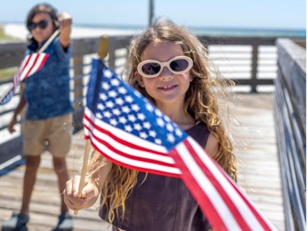 Kids waving American flags on a beachfront boardwalk in Gulf Shores