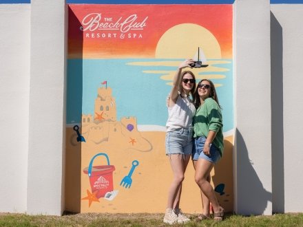 Two women posing in front of a mural at The Beach Club Resort in Fort Morgan