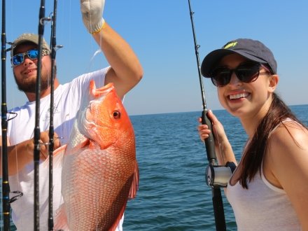 Angler and deck hand holding up red snapper caught on a fishing charter trip in Orange Beach