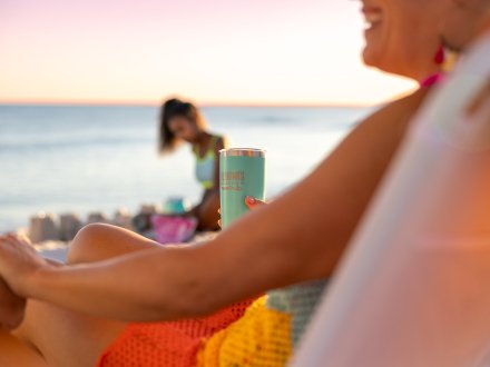 Woman holding a stainless steel cup under a beach umbrella by the shore