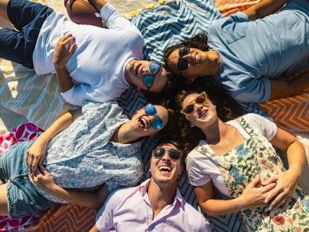 A group of friends wearing sunglasses laying on the beach in Gulf Shores