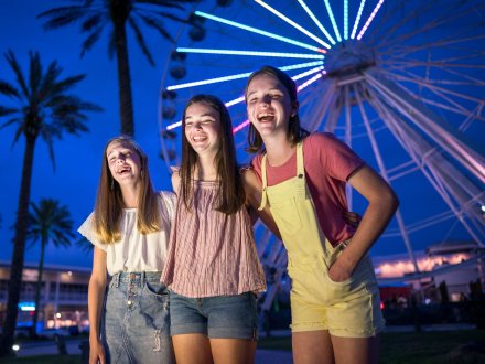 Teen girls laughing in front of the lighted Ferris Wheel at The Wharf