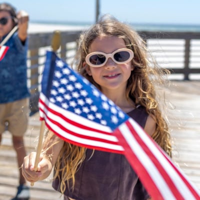 Kids waving American flags on a beachfront boardwalk in Gulf Shores