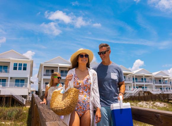 Happy family walking from beachfront vacation rentals to the beach on a sunny day at Alabama’s Beaches